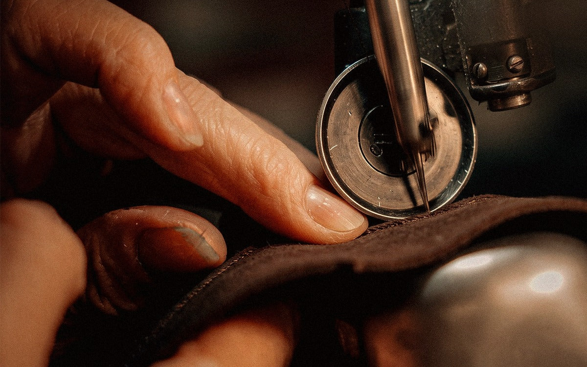 Mãos costurando um chapéu no ateliê — ofício e herança